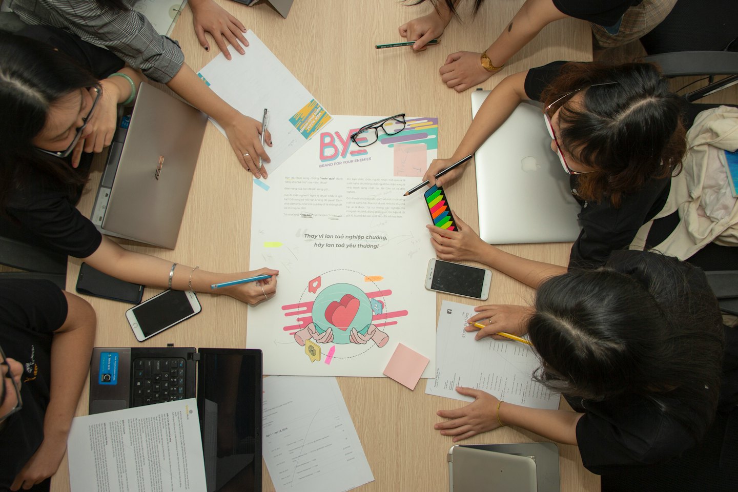 Un equipo colabora en un póster de diseño alrededor de una mesa.